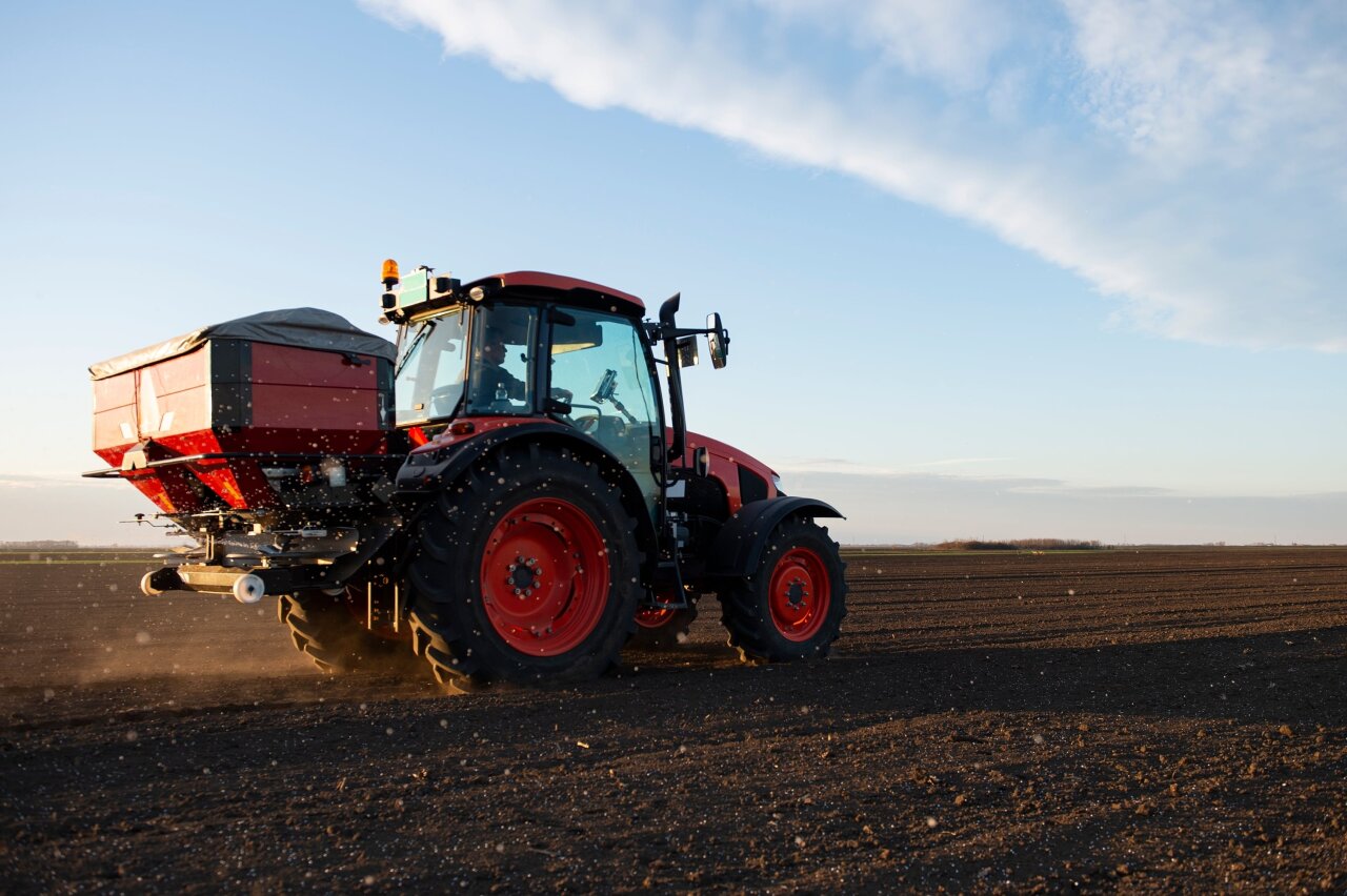 Rød traktor i full sving med å gjødsle jordåkeren i ettermiddagssolen.